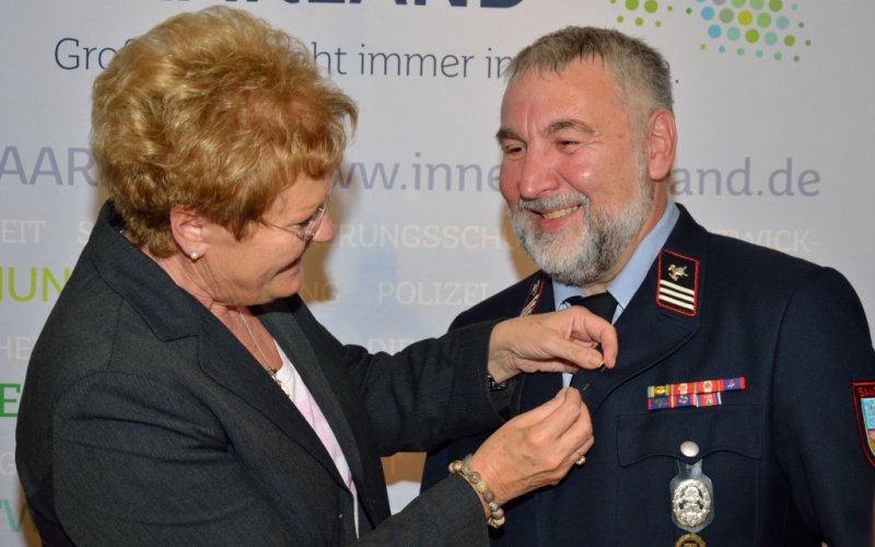 Die Ministerin steckt Johann Amann die saarländische Ehrenamtsnadel an.